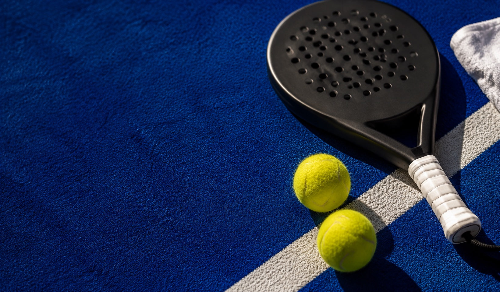 Sfeerbeeld van padelballen en een racket op een blauwe baan